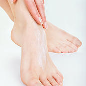 Close-up woman applying moisturizer cosmetic cream on foot on light background